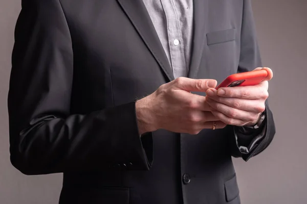 İş adamı elinde kırmızı çantalı bir telefon tutuyor.