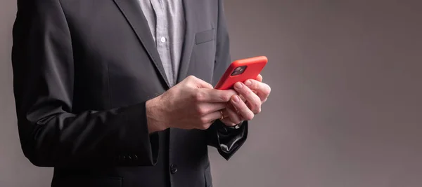 İş adamı elinde kırmızı çantalı bir telefon tutuyor.