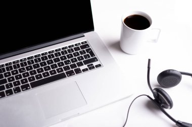 Ofis masasında bir fincan kahve bilgisayarı, kulaklık.