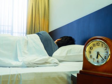 Yatakta uyuyan Asyalı bir adam ve masada bir el saati..