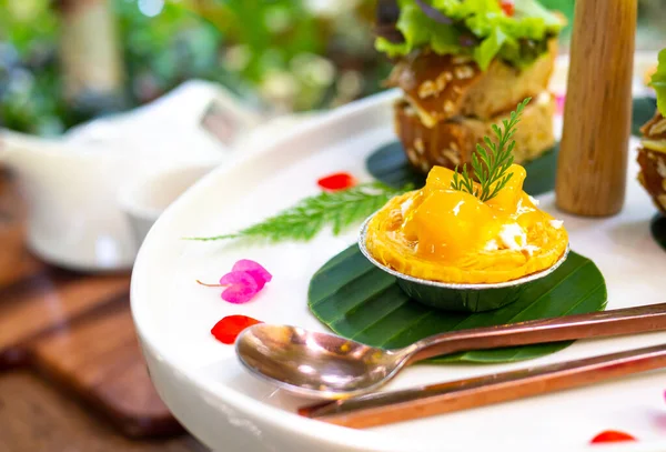 Mango tart mini beyaz bir tabakta servis edilir ve güzel çiçeklerle süslenir..