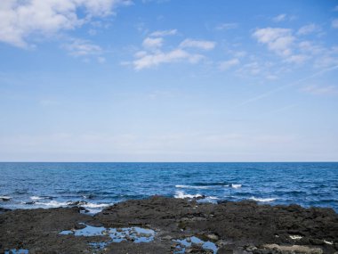 Kore 'deki Jeju adasının siyah kumlu ve gökyüzüyle güzel mavi deniz.