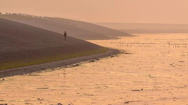 Persona caminando en dique de mar en neblina naranja —  Fotos de Stock