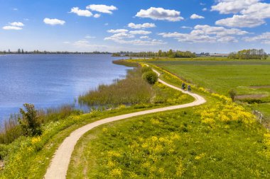 Boornzwaag yakınlarındaki Hollanda nehrinin havadan çekilmiş bir görüntüsü. Bisiklet pisti, sarı çiçeklerle gezen hendekte. Friesland, Hollanda.