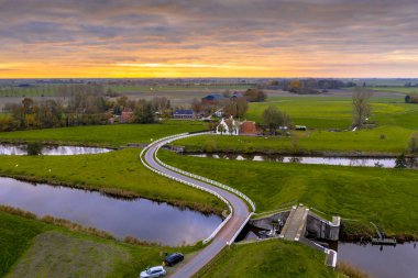 Hollanda 'nın kırsal kesiminde akşamları, Hollanda' nın Groningen Eyaleti 'nde beyaz çitli eğri bir yol üzerinde tarihi evlerin bulunduğu hava manzarası. Avrupa 'nın doğasında manzara manzarası.