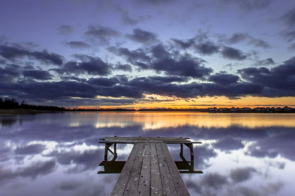 Pôr do sol roxo sobre molhe de madeira no lago tranquilo — Fotografia de Stock