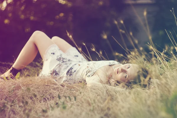 Piękna młoda kobieta leżąca na trawie w letnim zachodzie słońca — Zdjęcie stockowe