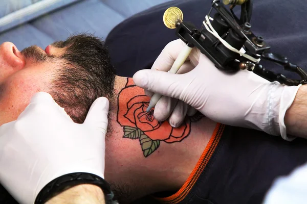 Tattooer showing process of making a tattoo. Tattoo design in the form of rose flower — ストック写真