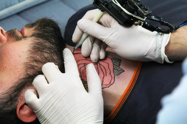 Tatuatore mostrando processo di fare un tatuaggio. Disegno del tatuaggio sotto forma di fiore di rosa — Foto Stock