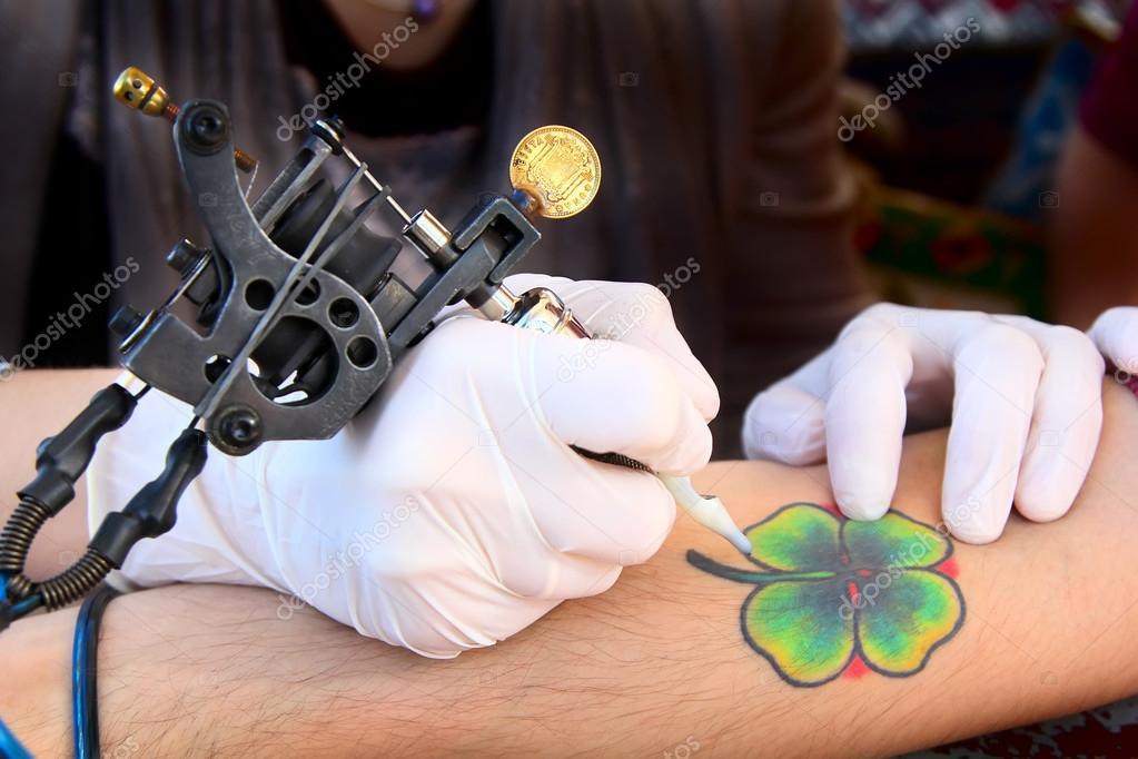 Tattooer showing process of making a tattoo. Tattoo design in the form of four-leaf clover