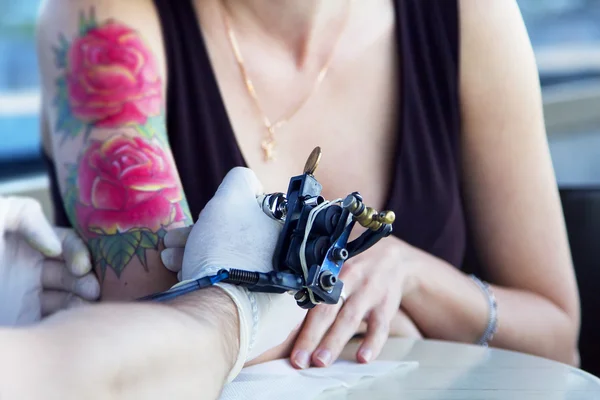 Tattooer showing process of making a tattoo on young beautiful hipster woman with red curly hair hand. Tattoo design in the form of rose — Stock Photo, Image