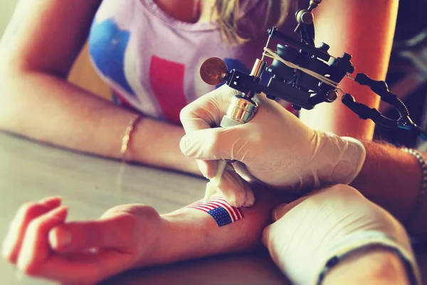 Tattooer showing process of making a tattoo on young beautiful hipster woman with blonde hair hand. Tattoo design in the form pin-up girl with flower head — 图库照片