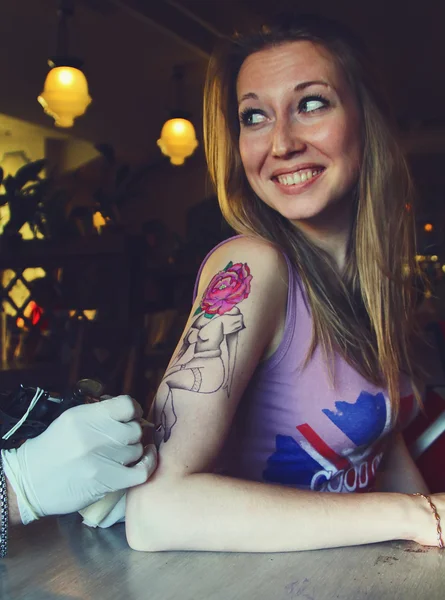 Tatuagem mostrando processo de fazer uma tatuagem em jovem bela mulher hipster com mão de cabelo loiro. Design de tatuagem na forma pin-up menina com cabeça de flor — Fotografia de Stock