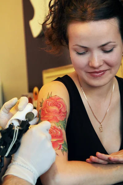 Tatuador mostrando el proceso de hacer un tatuaje en la joven hermosa mujer hipster con el pelo rizado rojo. Diseño del tatuaje en forma de rosa — Foto de Stock