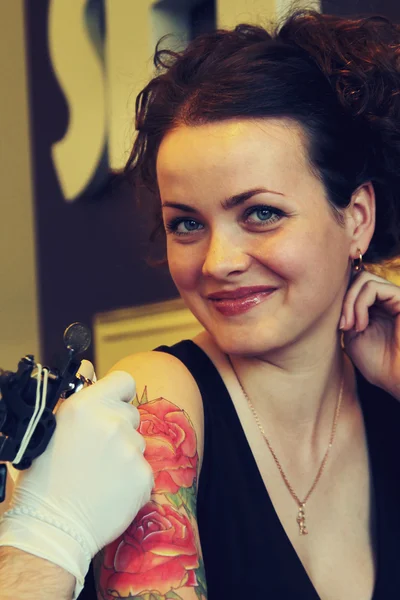 Татуировщик, показывающий процесс создания татуировки на молодой красивой хипстерской женщине с рыжими вьющимися волосами. Татуировка в виде розы — стоковое фото