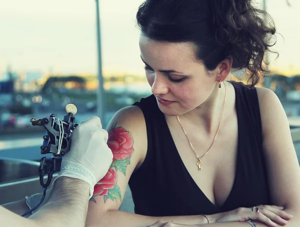 Tattooer showing process of making a tattoo on young beautiful hipster woman with red curly hair . Tattoo design in the form of rose — Stock Photo, Image