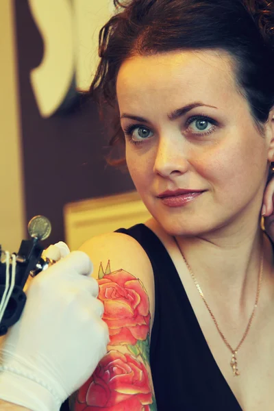 Tattooer showing process of making a tattoo on young beautiful hipster woman with red curly hair . Tattoo design in the form of rose — Stock Photo, Image