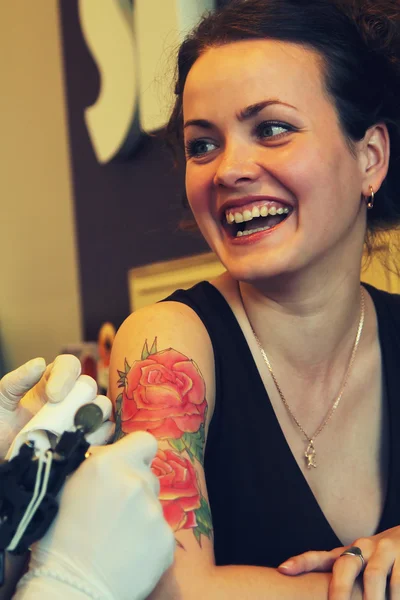 Tattooer showing process of making a tattoo on young beautiful hipster woman with red curly hair . — Stock Photo, Image