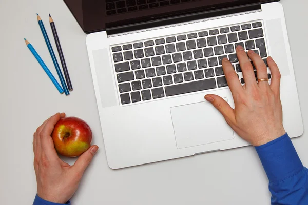 Man holding an apple , and prints on the laptop keyboard — Stock Photo, Image