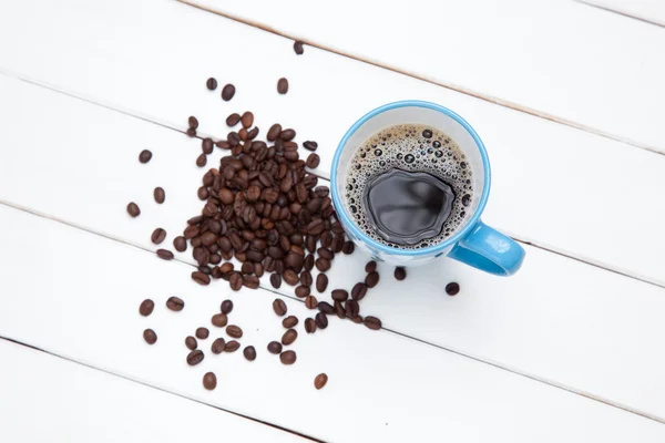 Tasse Kaffee und Bohnen auf weißem Holztisch — Stockfoto