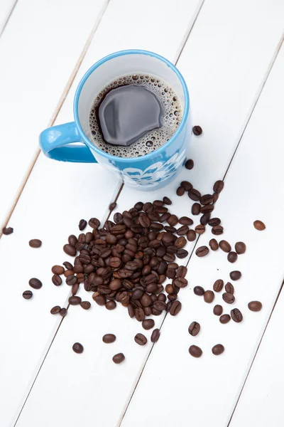 Nahaufnahme einer Tasse Kaffee und Bohnen auf weißem Holztisch — Stockfoto