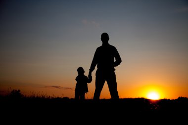 Gün batımında el ele tutuşan baba ve oğulun silueti.