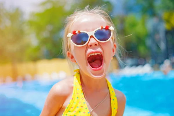 Niña con gafas de sol cerca de la piscina gritando de felicidad. Vacaciones de verano. concepto de oliday — Foto de Stock