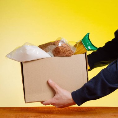 Bağış kutusunda, sarı arka planda yiyecekleri olan bir gönüllü. kare resim