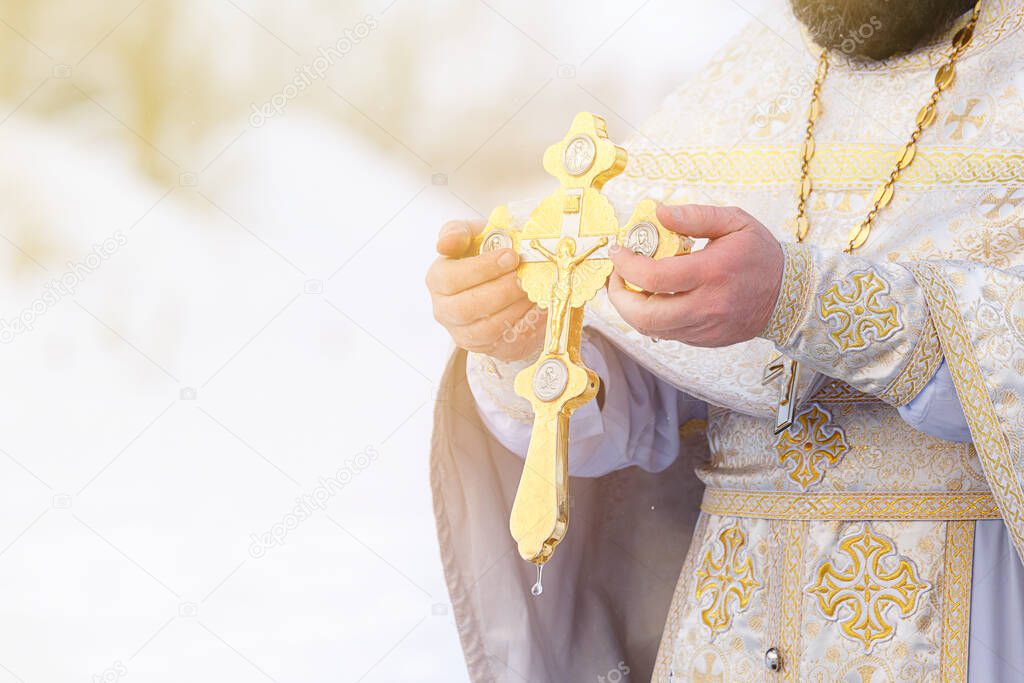 The hands of a priest dip an Orthodox gold cross into the river. Feast of the Epiphany of Russia.