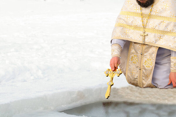 The priest sanctifies the water cross in the hole on the feast of the Baptism of the Lord. Traditional rite of consecration of water on Epiphany.
