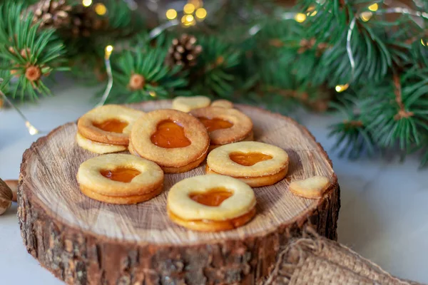 Christmas linzer cookie with apricot jam and spruce branches on wooden saw cut. — Stock Photo, Image