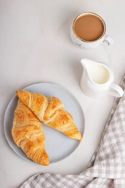 Fresh french croissants on plate, cup of coffee and milkman in the morning light. Continental morning breakfast on marble background. — Stock Photo, Image