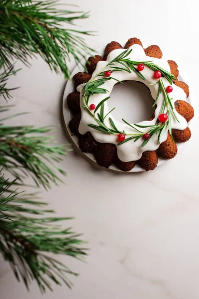 Gâteau Bundt de Noël avec glaçure blanche et branches d'épinette sur fond clair. Vue du dessus. — Photo