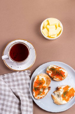 Kırmızı havyarlı sandviçler ve kahverengi arka planda bir fincan çay.. 