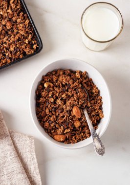 Beyaz bir tabakta, arka planda süt bulunan ev yapımı çikolatalı granola. Sağlıklı kahvaltı.