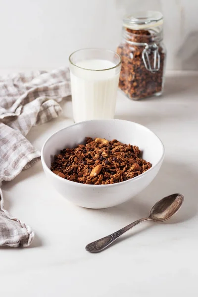 Beyaz bir tabakta, arka planda süt bulunan ev yapımı çikolatalı granola. Sağlıklı kahvaltı.