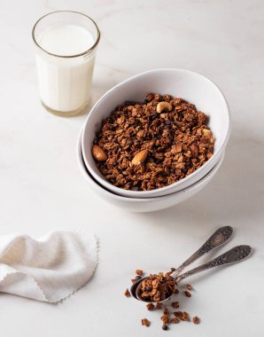 Beyaz bir tabakta, arka planda süt bulunan ev yapımı çikolatalı granola. Sağlıklı kahvaltı.