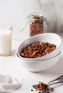 Beyaz bir tabakta, arka planda süt bulunan ev yapımı çikolatalı granola. Sağlıklı kahvaltı.