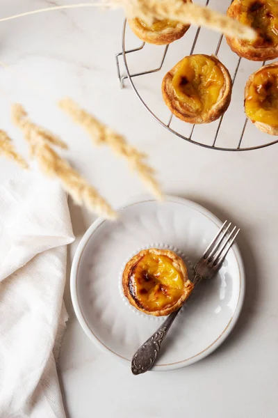 Pastel de Nata - beyaz mermer arka planda Portekiz yumurtalı muhallebi. Seramik tabakta çatallı Portekiz börekleri