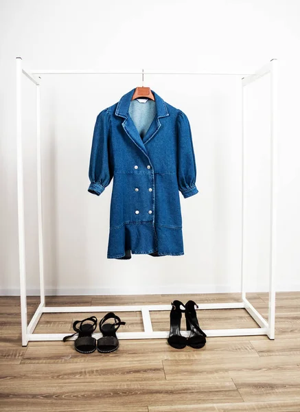Fashionable denim dress hanging on hanger and sandals — Stock Photo, Image