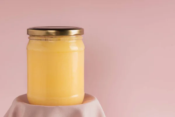 Ghee oder geklärte Butter im Glas auf rosa Hintergrund. Minimaler Stil. Szene mit geometrischen Formen. Kopierraum. — Stockfoto