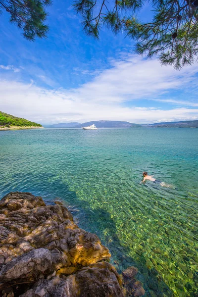 Hombre joven nadando en la playa de piedra con turquesa cristalina s —  Fotos de Stock