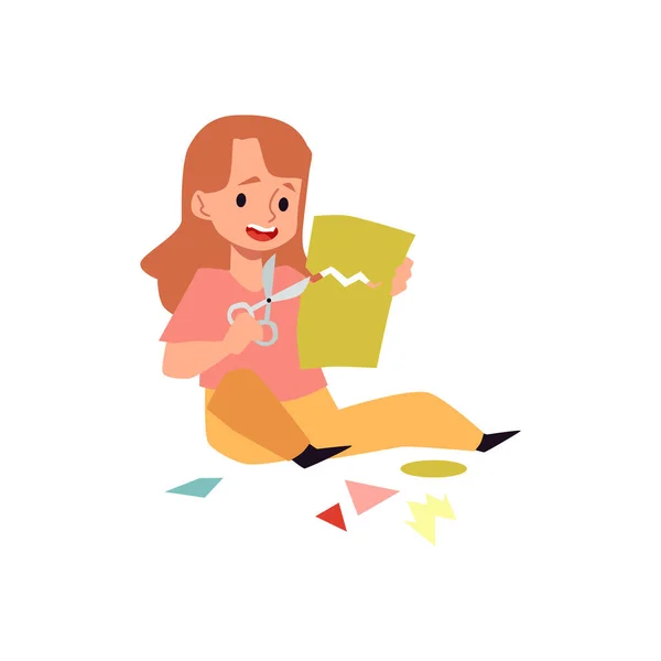 Menina bonito sentado no chão e papel cor de corte com tesoura. —  Vetores de Stock