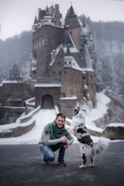 Bir adam ve bir köpek kışın kalenin arka planında birlikte. Doğada Avustralya çobanı