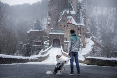 Bir adam ve bir köpek kışın kalenin arka planında birlikte. Doğada Avustralya çobanı