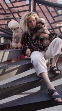 Beyaz elbiseli bir kadın iki tarafında kaniş olan açık hava merdivenlerinde oturuyor. Modern şehir ortamı rahatlatıcı, kentsel bir ortam sağlıyor..