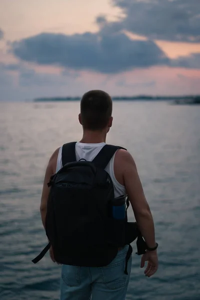 A man looks at the sea and the sunset. A man with a backpack looks at the sea and a beautiful sunset