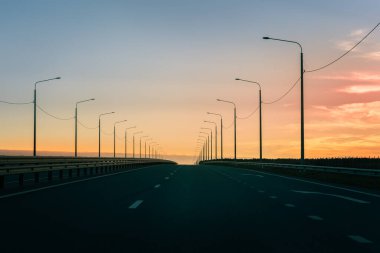 Gün batımında otoyol. Gün batımına giden yol. Gün batımına doğru giden sokak lambaları olan boş bir otoyol..