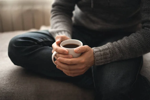 Elinde kahve olan bir adam. Pencerenin yanında oturan bir adam kahve içer.