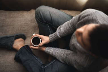 Elinde kahve olan bir adam. Pencerenin yanında oturan bir adam kahve içer.